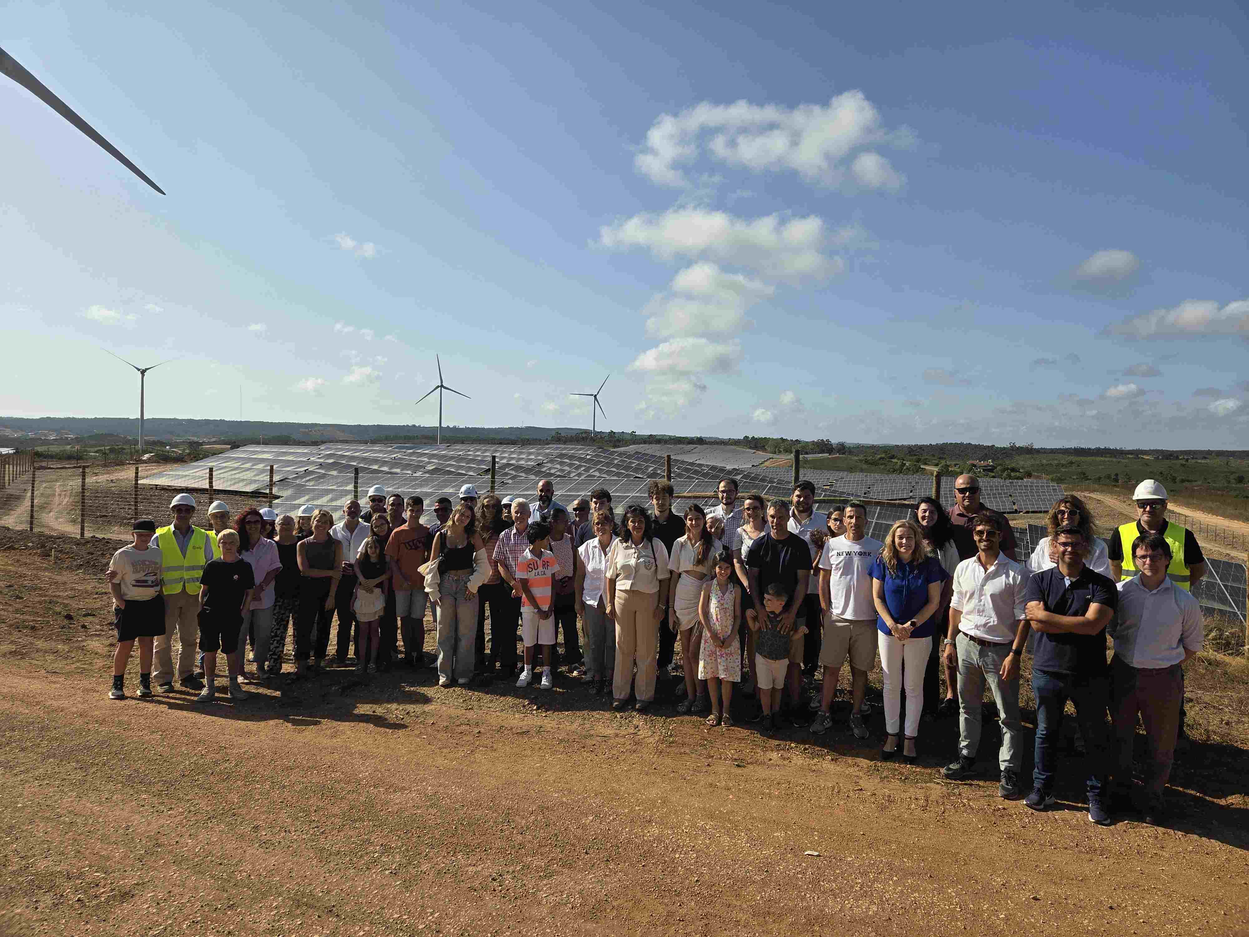 Grupo de personas posando para una foto frente a un parque de instalaciones solares y algunos molinos de viento