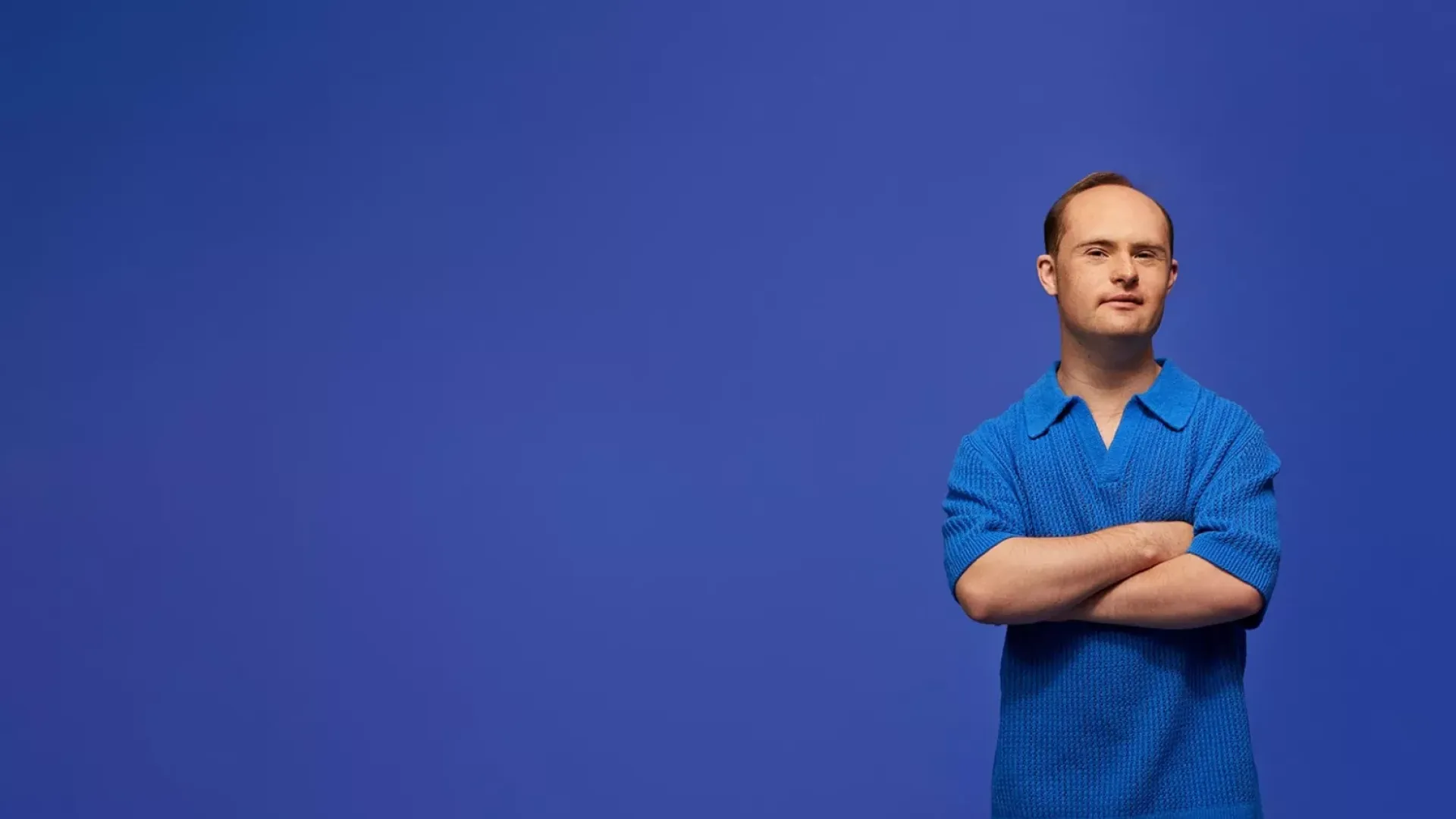 Man standing with arms crossed in front of a blue background.