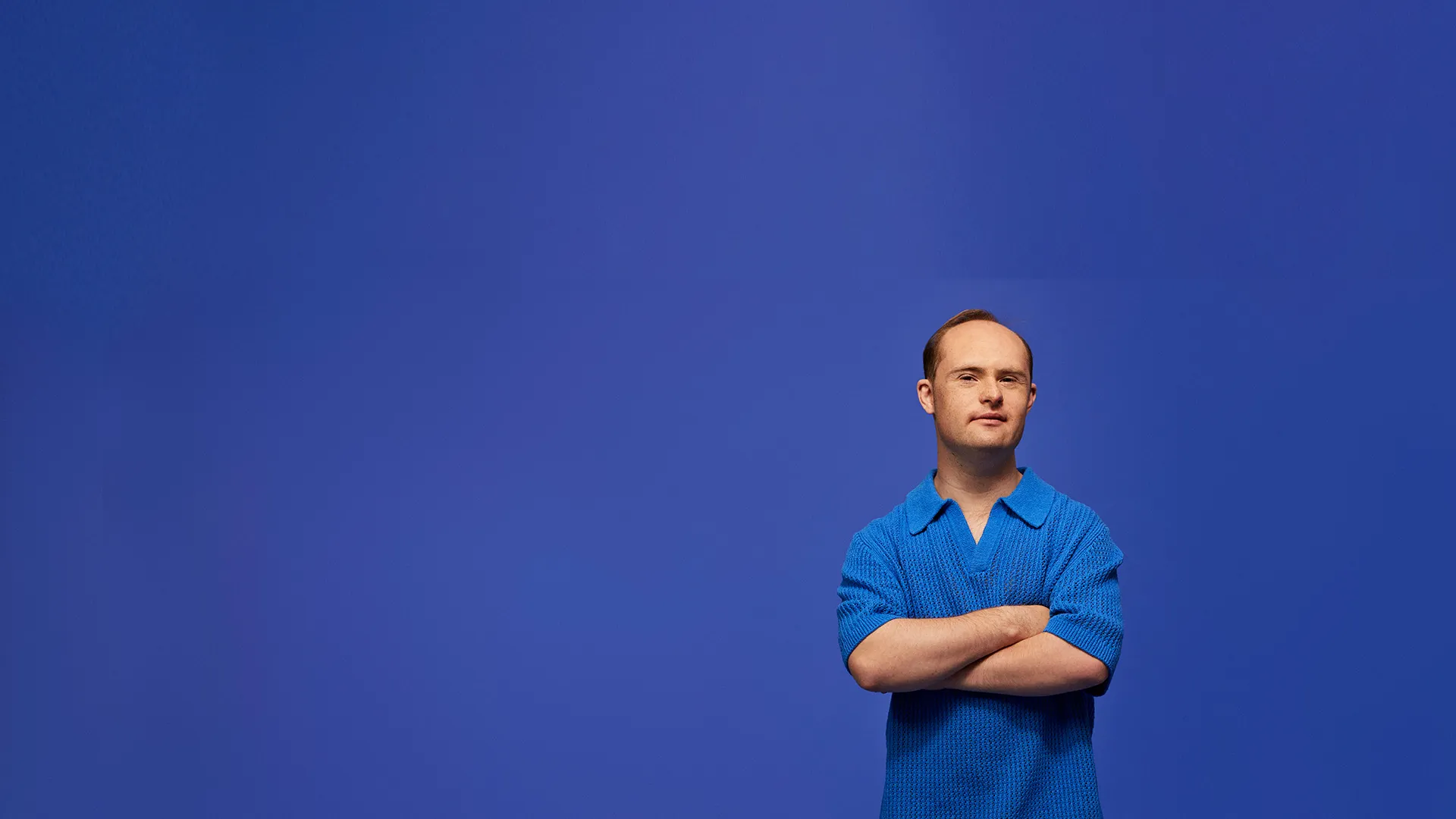 Man standing with arms crossed in front of a blue background.