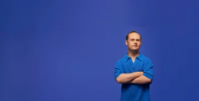 Man standing with arms crossed in front of a blue background.